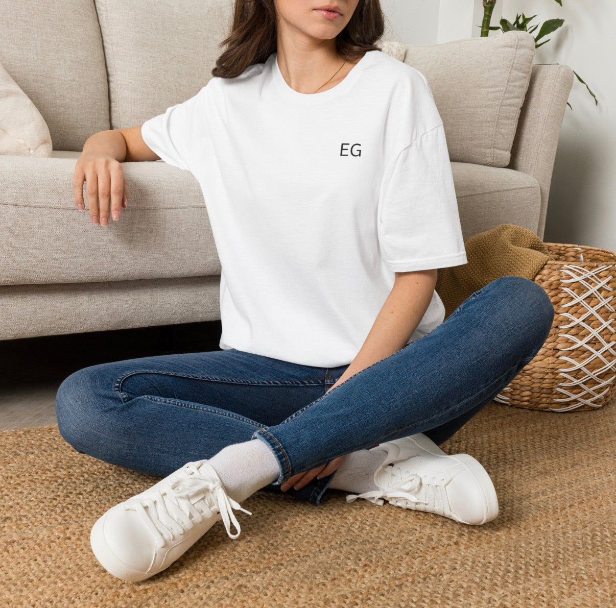 Model wearing a white unisex softstyle t-shirt, sitting casually on a rug in a cozy living room.